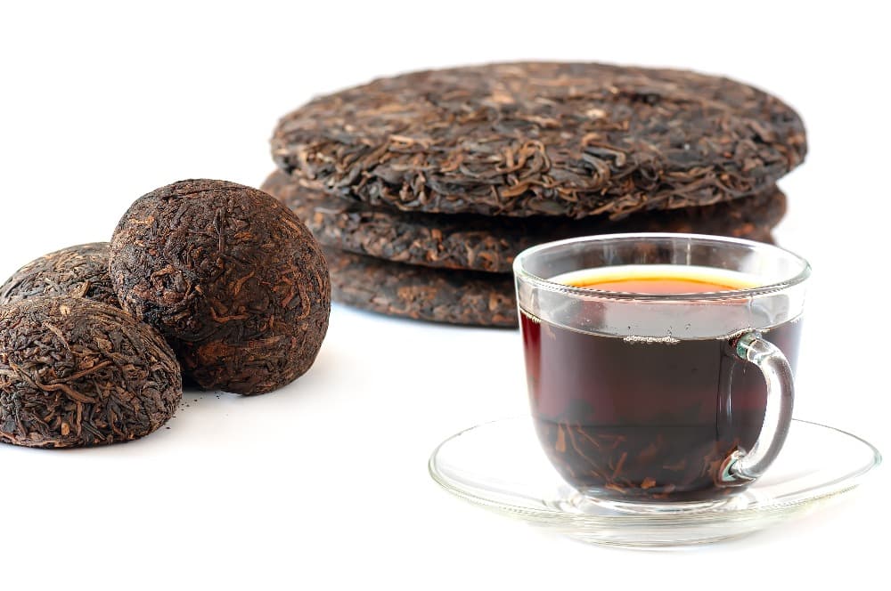 Glass cup of dark tea with stacked and round compressed tea leaves.
